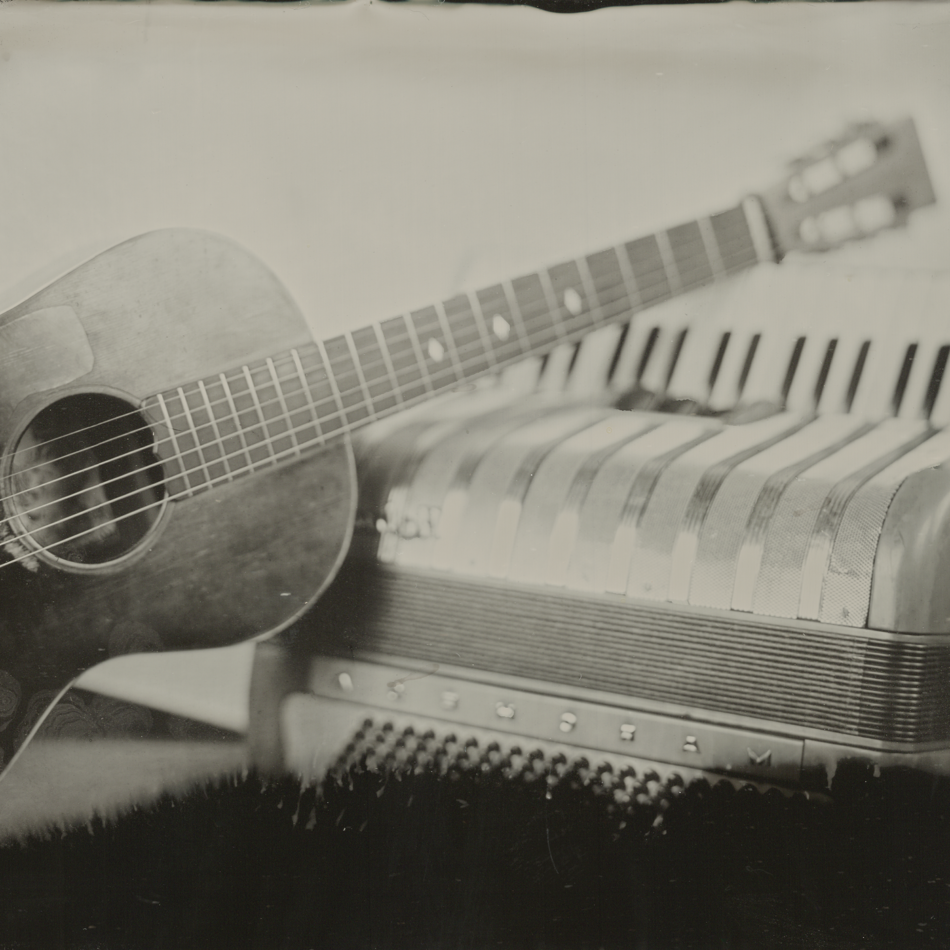 Black and white tintype of an acoustic guitar and an accordion